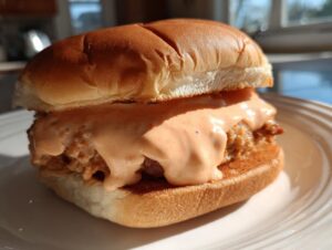 A juicy burger generously topped with creamy, orange-hued burger sauce, served on a white plate.