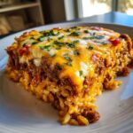 A close-up of a hearty slice of burrito bake, layered with seasoned meat and rice, topped with melted cheddar and Monterey Jack cheese and fresh parsley.