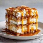 A close-up of a layered slice of caramel apple trifle topped with whipped cream and rich caramel sauce dripping down the sides.