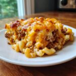 A generous serving of baked cheeseburger casserole featuring elbow macaroni, ground beef, and a bubbly, browned cheddar cheese topping.