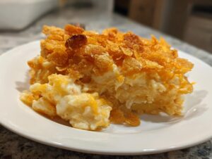 A generous serving of creamy, cheesy potato casserole topped with crispy, golden cornflakes on a white plate.