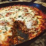 Close-up of a bubbling skillet lasagna topped with melted mozzarella cheese and parsley, with a serving removed.