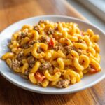 A close-up of creamy, cheesy taco pasta mixed with ground beef and diced tomatoes served on a white plate.