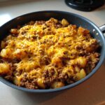 Close-up of Cheesy Taco Potatoes cooked in a black skillet, topped with melted shredded cheddar cheese.