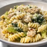 A close-up of a bowl filled with creamy chicken caesar pasta salad featuring rotini pasta, grilled chicken pieces, and romaine lettuce.