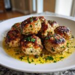 A plate of browned chicken piccata meatballs swimming in a bright lemon-butter sauce, garnished with parsley and capers.