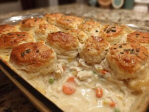 Close-up of golden biscuits topping a creamy chicken pot pie casserole with visible carrots and peas.