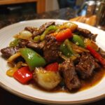 A close-up of vibrant Chinese pepper steak featuring tender beef, green and red bell peppers, and onions coated in a rich brown sauce.