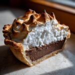Close-up of a slice of chocolate meringue pie showing the flaky crust, rich chocolate filling, and peaks of toasted meringue.