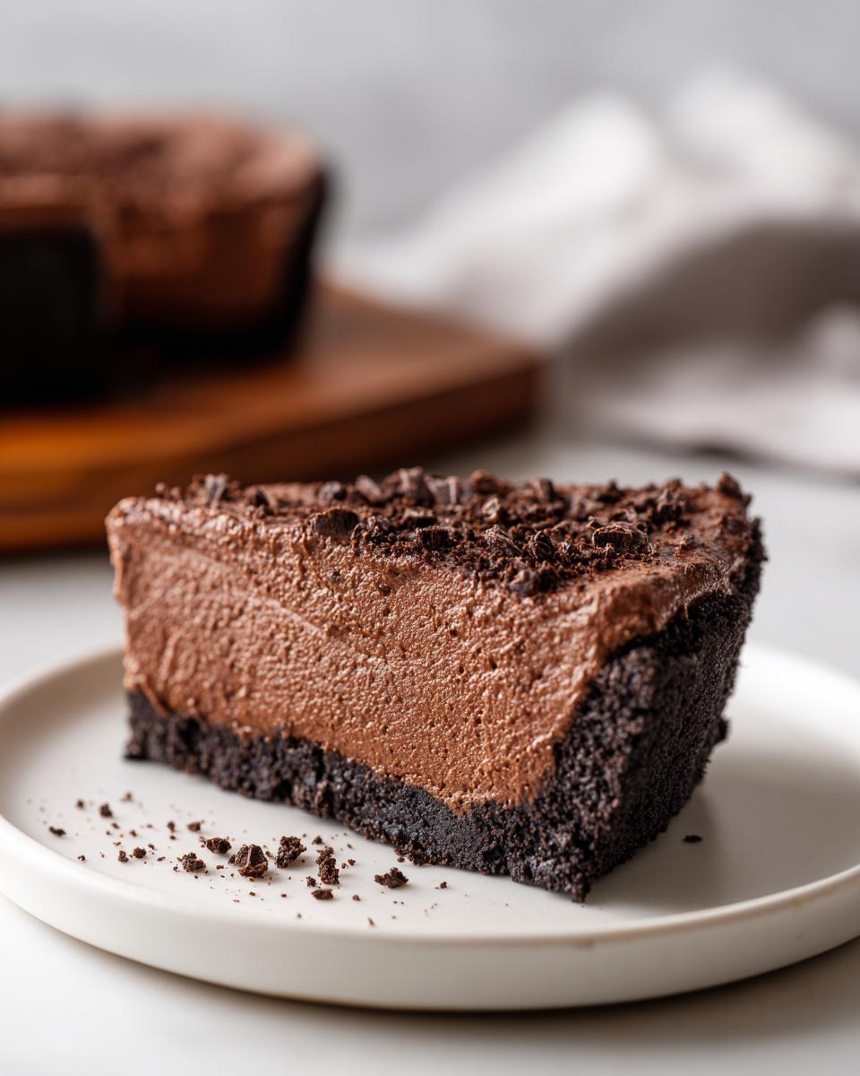 A thick slice of creamy chocolate mousse pie with a dark cookie crust, topped with chocolate shavings.