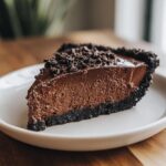 A decadent slice of chocolate mousse pie featuring a thick, airy filling and a dark chocolate crumb crust and topping.
