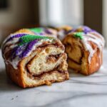 A cross-section view of a homemade king cake showing cinnamon swirl filling, white icing, and purple, green, and gold sprinkles.