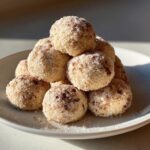 A stack of freshly made cinnamon sugar snowball cookies coated in sugar and sprinkled with cinnamon.