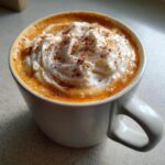 Close-up of a creamy pumpkin spice latte topped with whipped cream and cinnamon dusting.