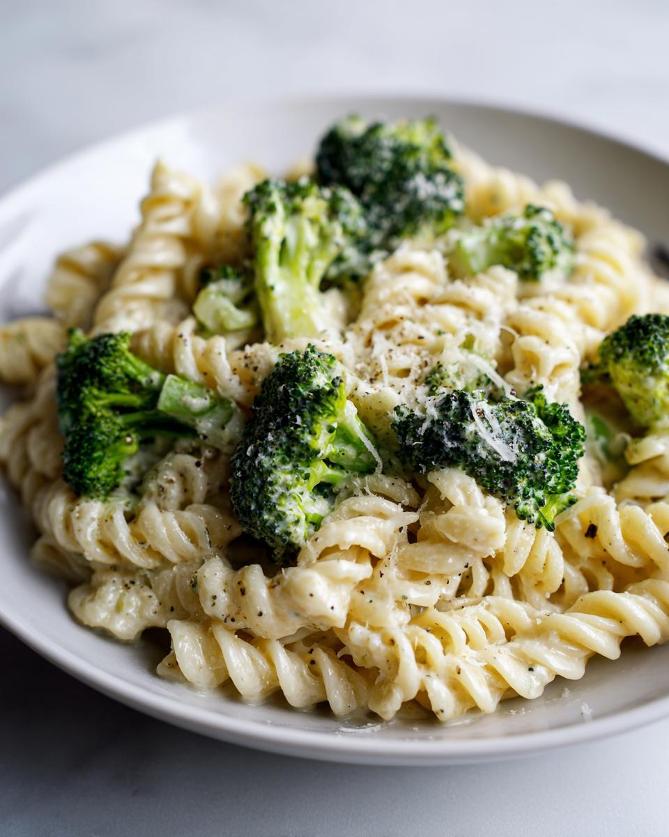 Close-up of creamy broccoli pasta made with fusilli noodles, topped with fresh broccoli florets and grated cheese.