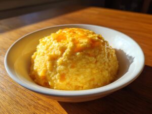 A white bowl filled with creamy, bright yellow cheese grits topped with melted cheese or butter.