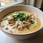 A close-up of a creamy white chicken chili recipe bowl topped with shredded chicken, sour cream, and fresh cilantro.