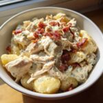 A close-up of a white bowl filled with creamy crack chicken gnocchi topped with crispy bacon bits and black pepper.