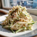 A mound of creamy kani salad mixed with shredded crab and julienned cucumber served on a white plate.