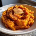 A close-up of creamy, bright orange mashed sweet potatoes topped with a pat of melting butter and a dusting of cinnamon.
