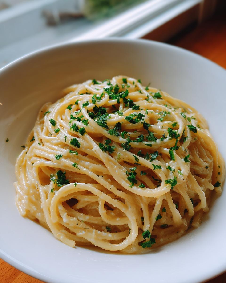 A close-up of creamy parmesan pasta tossed in a rich sauce and topped with fresh chopped parsley in a white bowl.