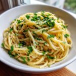 A close-up, appetizing shot of creamy parmesan pasta tossed with fresh parsley and black pepper in a white bowl.