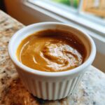 Close-up of rich, creamy peanut sauce swirled inside a small white ramekin.