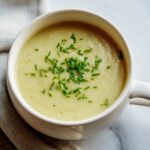 A close-up of creamy potato leek soup in a white mug, topped generously with fresh, chopped chives.
