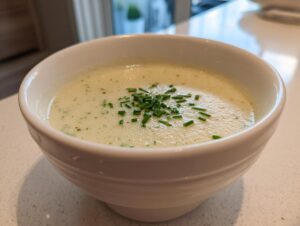 Close-up of a white bowl filled with creamy potato leek soup, topped with fresh chopped chives.