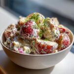 Close-up of a creamy red potato salad in a speckled bowl, topped generously with fresh dill.