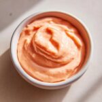 Close-up of creamy, orange-pink smash burger sauce swirled in a small white dipping bowl.
