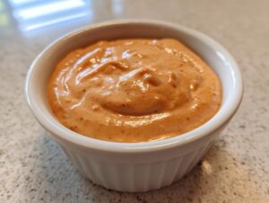 Close-up of creamy, orange-hued smash burger sauce served in a small white ramekin.