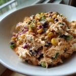 Close-up of creamy, shredded southwest chicken salad mixed with corn, black beans, and red onion in a white bowl.