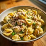 Close-up of creamy tuna pasta shells mixed with bright green peas and topped with grated cheese.