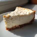 A thick, creamy slice of white chocolate cheesecake with a graham cracker crust sitting on a white plate.