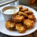 A plate piled high with golden brown, crispy Fried Pickles served next to a small white ramekin of seasoned dipping sauce.