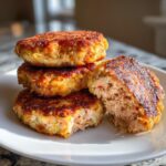 A stack of four golden-brown, crispy salmon cakes, with one cut open to show the flaky salmon interior.
