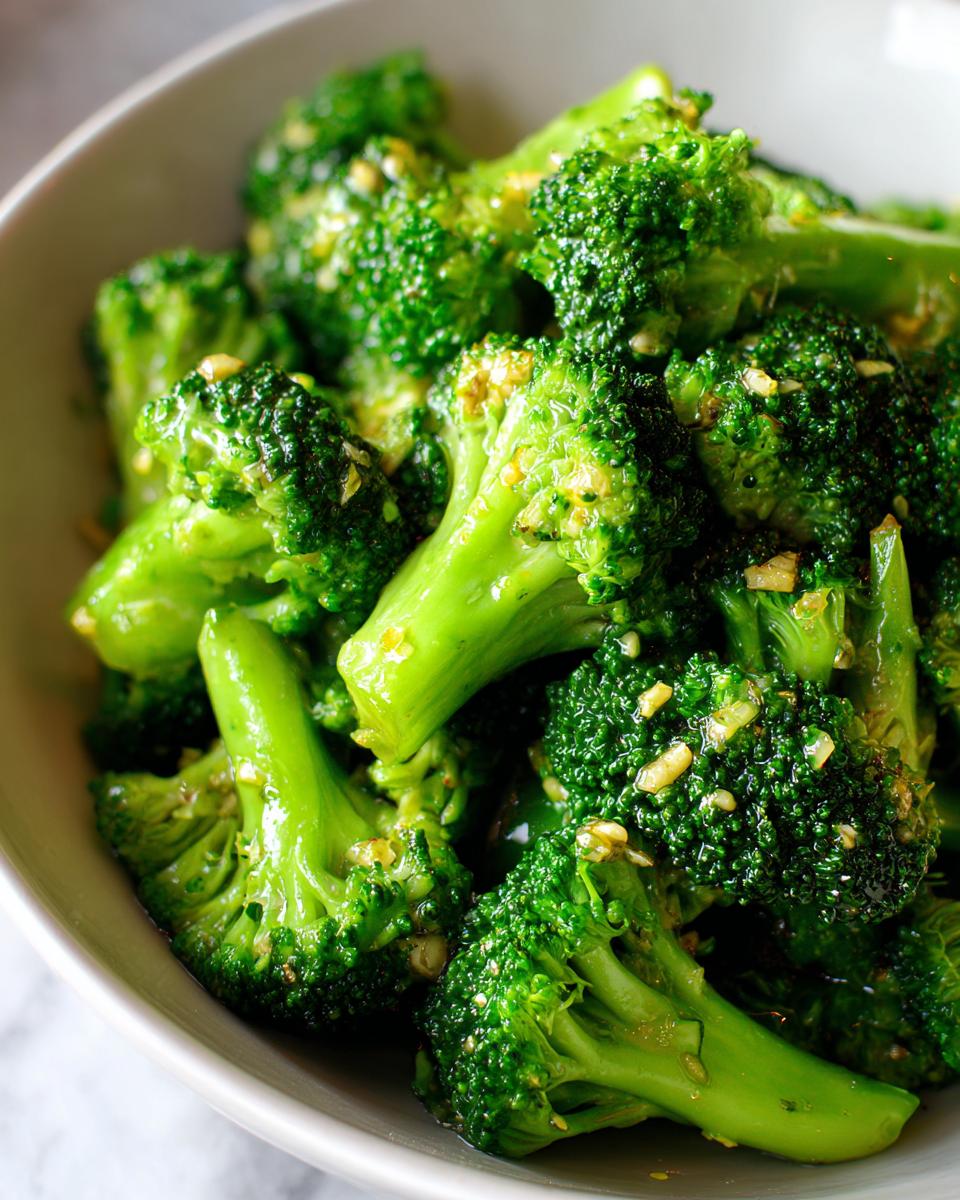 Close-up of vibrant green steamed broccoli florets tossed with minced garlic served in a light-colored bowl.