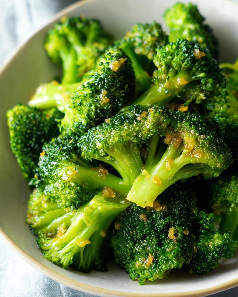 Close-up of vibrant green, perfectly steamed broccoli florets topped with minced garlic.