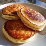 Three thick, fluffy almond flour pancakes with golden-brown, perfectly seared tops served on a white plate.
