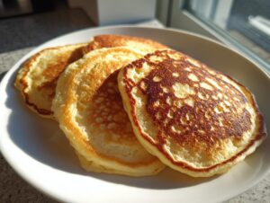 Close-up of three fluffy almond flour pancakes stacked on a white plate, perfectly golden brown.