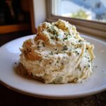 A generous serving of creamy boursin mashed potatoes topped with fresh chopped chives on a white plate.