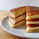 Close-up of a thick stack of fluffy coconut flour pancakes, cut to show the airy interior and drizzled with syrup.