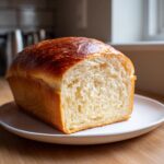 A freshly baked loaf of soft condensed milk bread, sliced to show its fluffy interior and golden brown crust.