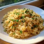 A close-up of fluffy, golden rice pilaf topped with chopped fresh parsley in a white bowl.
