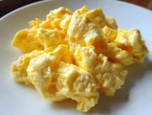 A close-up of rich, yellow, fluffy scrambled eggs served on a white plate.