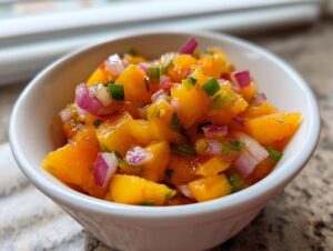 Close-up photo of vibrant, chunky peach salsa featuring diced peaches, red onion, and green peppers in a small white bowl.