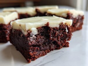 A close-up view of a rich, dark gingerbread brownies square topped with thick white cream cheese frosting.