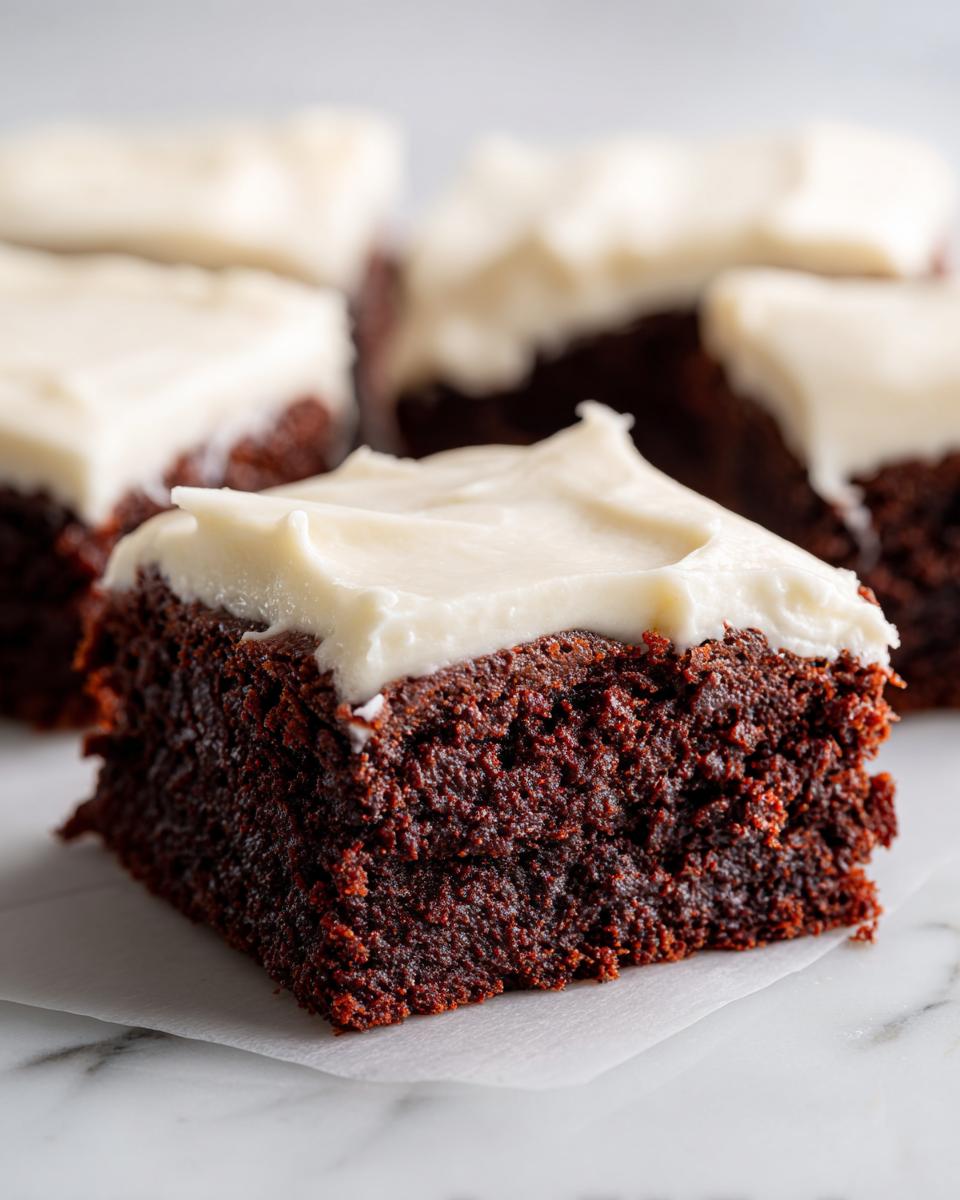 A close-up of a rich, dark square of gingerbread brownies topped with thick, creamy white frosting.