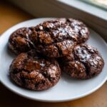 A stack of five fudgy brownie cookies featuring shiny, cracked tops, served on a white plate.